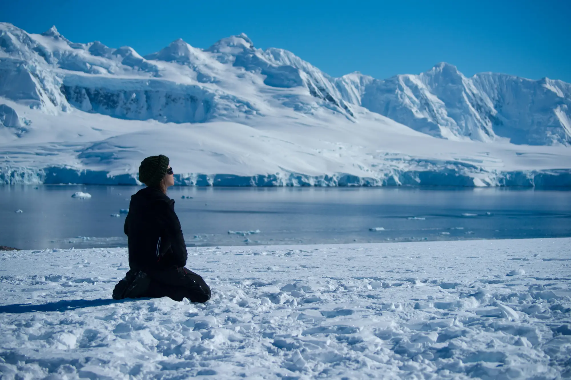 An explorer sitting on the ice-covered ground of Antarctica.